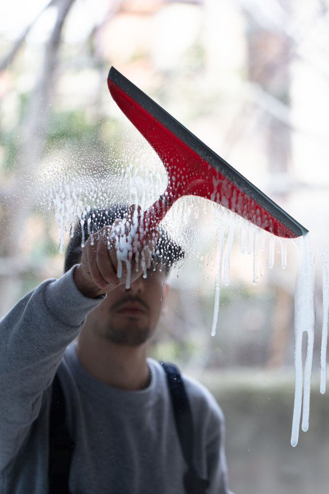 Closeup of a person cleaning windows with a red squeegee